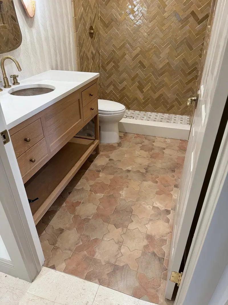 Baño con un tocador de madera, un piso de azulejos rosados y terracota con formas, y la ducha en espiga al fondo