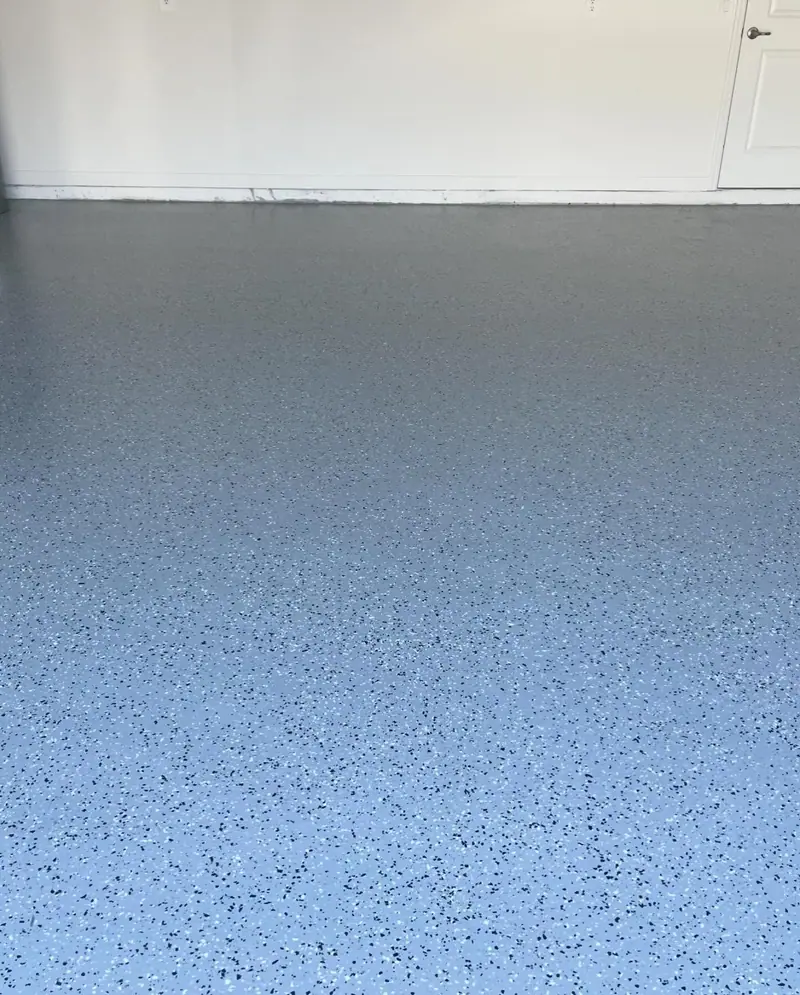 Piso epóxico gris de garaje con motas negras y blancas, hasta una pared blanca y una puerta interior