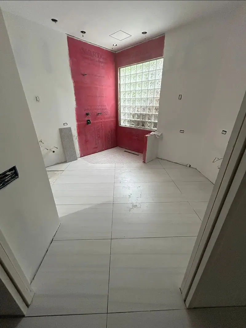 Placas de cemento rojas en las paredes de la ducha alrededor de la ventana de bloques de vidrio, con el azulejo grande del piso ya colocado