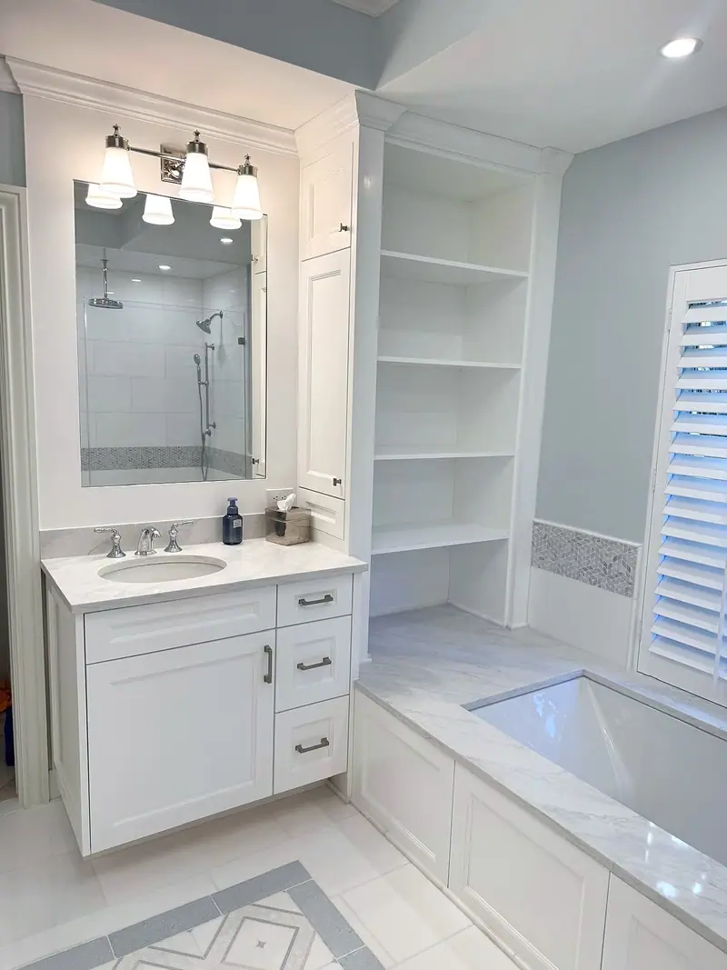 White shaker vanity under a four-light fixture, with built-in open shelves beside it and the tub in front