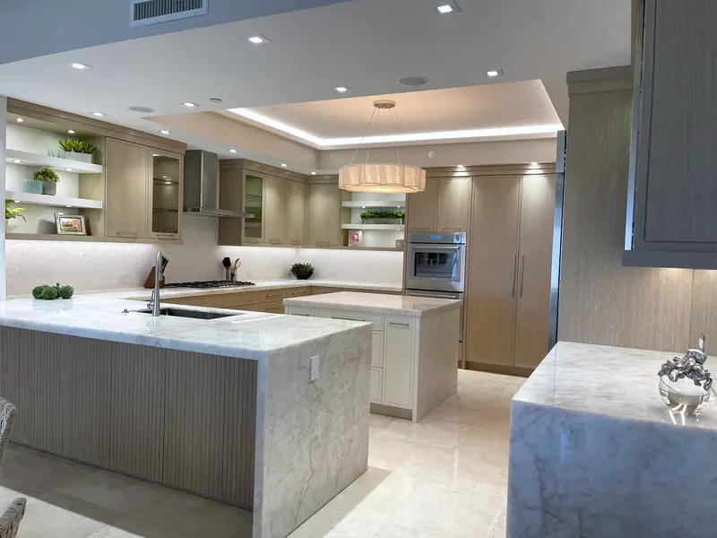 Cocina con dos islas de piedra en cascada, gabinetes de roble y un techo escalonado iluminado