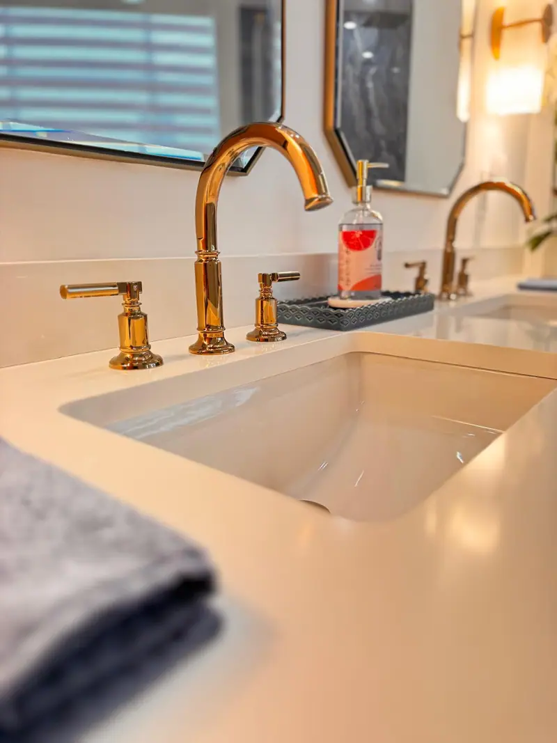 Primer plano de un grifo de latón pulido sobre una encimera blanca con un lavabo empotrado