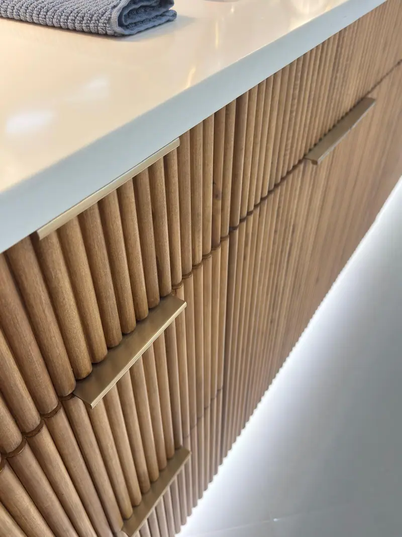 Primer plano de frentes de cajones de madera acanalada con tiradores de borde de latón e iluminación debajo