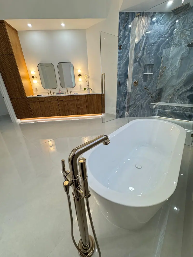 Bañera independiente con una grifería de piso pulida, con el tocador de madera y la ducha azul detrás