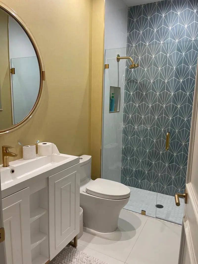 Medio baño con una pared dorada, un espejo redondo de latón y azulejos azules con dibujo en la ducha