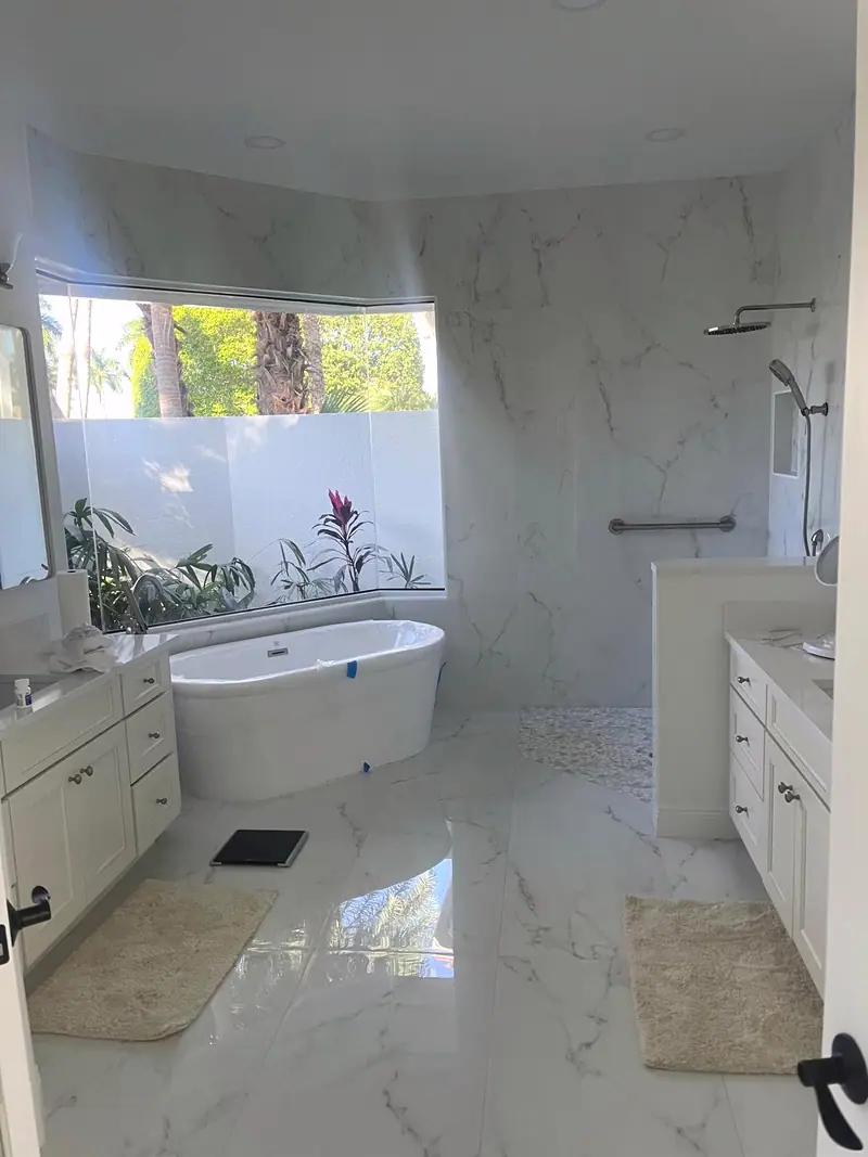 Baño principal con azulejos blancos veteados, bañera independiente y ventana al jardín